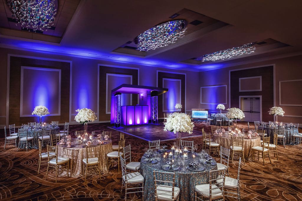 ballroom of Margaritaville Resort Orlando with dj setup, purple uplights, and silver and gold decorations for the tables
